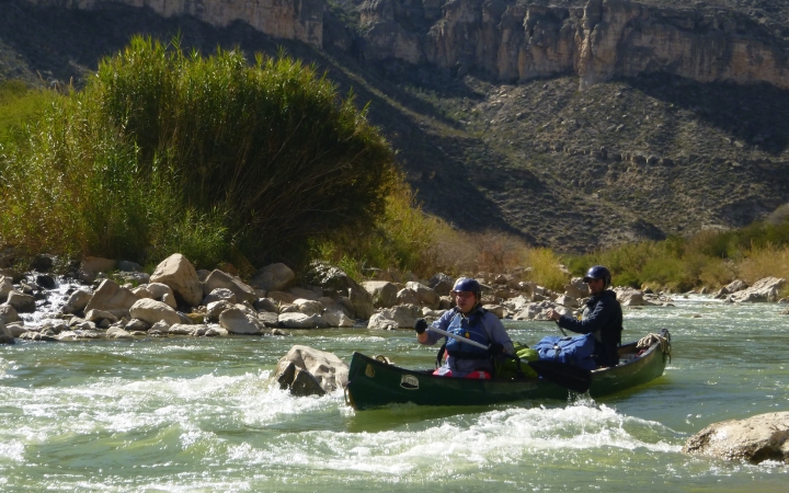 two people in a canoe navigate whitewater on an outward bound veterans trip
